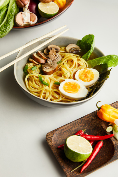 tradycyjny azjatycki ramen w misce koło pałeczek, warzywa na szarej powierzchni - Zdjęcie, obraz