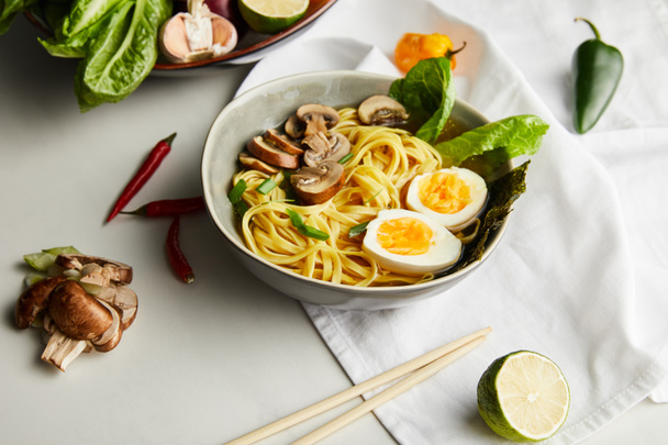 traditional asian ramen in bowl near chopsticks, napkin and vegetables on grey surface - Foto, Imagem