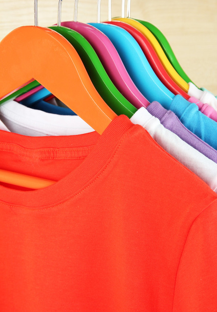 Different shirts on colorful hangers on light background - Foto, Bild