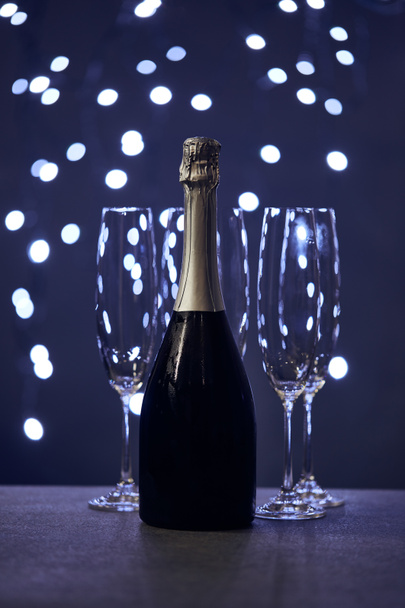 μπουκάλι αφρώδες κρασί και ποτήρια με μπλε χριστουγεννιάτικα φώτα bokeh - Φωτογραφία, εικόνα
