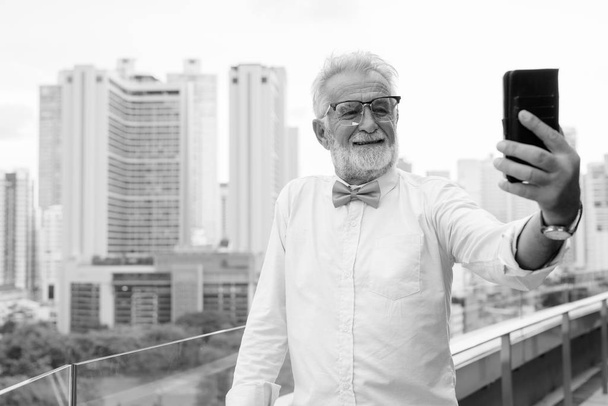 Przystojny brodaty starszy turysta zwiedzający miasto w czerni i bieli - Zdjęcie, obraz