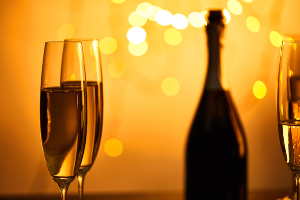 glasses of sparkling wine with blurred bottle and yellow christmas lights - Foto, afbeelding