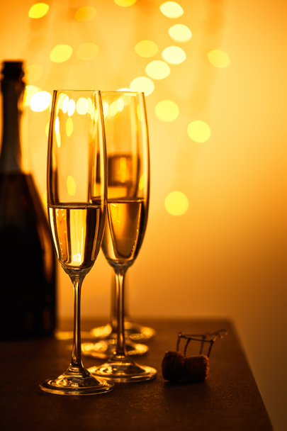 cork, bottle and glasses with sparkling wine, with yellow christmas lights bokeh - Fotó, kép