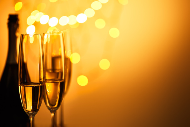 黄色のクリスマスライトとスパークリングワインのグラスとボトルボケ - 写真・画像