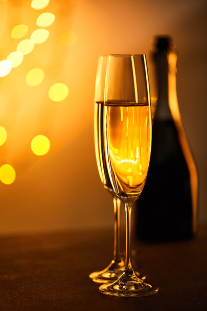 склянки шампанського з розмитою пляшкою і жовтими вогниками криштм. - Фото, зображення