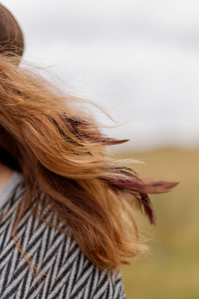cropped view of female red hair with feathers decoration blowing in wind outdoor  - Foto, Bild