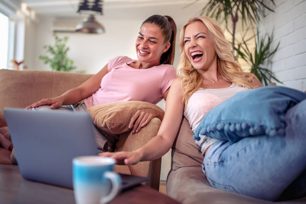 Fröhliche Mädchen schauen sich Filme auf Laptops an und trinken Kaffee. Konzept der Freizeit und Freundschaft. - Foto, Bild