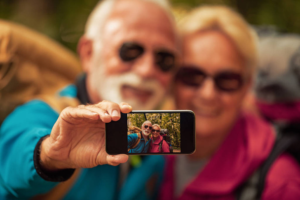 Happy senior couple walking together in a forest,taking selfie. - Foto, immagini