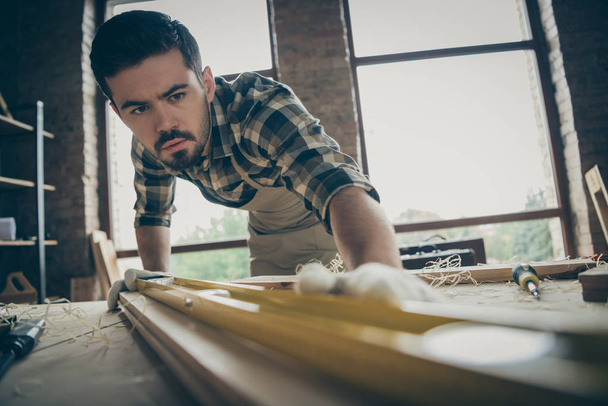 Close-up portrait of his he nice attractive serious focused hardworking expert repairman checking smoothness plank creating new house building start-up project at modern industrial loft style interior - 写真・画像