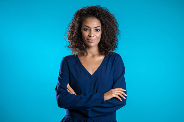 Atractiva mujer afroamericana con cabello afro en ropa de negocios sonriendo a la cámara sobre fondo azul de la pared. Linda raza mixta niñas retrato
 - Foto, imagen