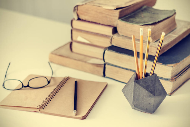 Stack of old books, textbook, glasses and pencils in office back - Фото, изображение