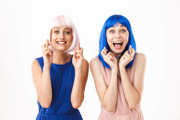Porträt zweier aufgeregter, glücklicher Frauen mit blauen und rosa Perücken, die zum Glück die Daumen drücken - Foto, Bild