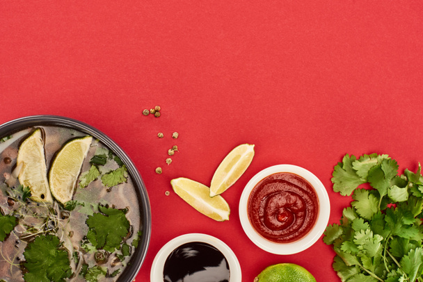 top view of pho in bowl near lime, chili and soy sauces and coriander on red background - Foto, Imagem
