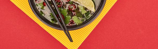 top view of pho in bowl with chopsticks, lime, chili and coriander on red and yellow background, panoramic shot - Photo, Image