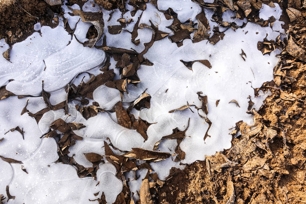 Przełamane lody na wiejskiej drodze. Zamrażająca kałuża i opadnięte liście. Streszczenie tła - Zdjęcie, obraz