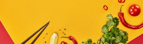 vrchní pohled na hůlky, vápno, chilli a koriandr na červeném a žlutém pozadí, panoramatický záběr - Fotografie, Obrázek