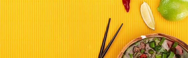 πάνω άποψη του pho σε μπολ κοντά chopsticks, ασβέστη, τσίλι σε κίτρινο υφή φόντο, πανοραμική λήψη - Φωτογραφία, εικόνα