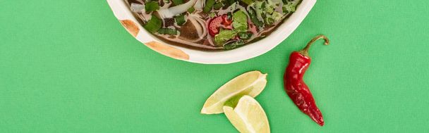 top view of pho in bowl near lime, chili on green background, panoramic shot - Foto, immagini
