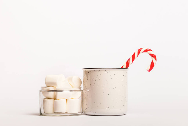 Рождественская композиция с кружкой горячего какао с зефиром. Кружка какао с тростниковыми конфетками и зефиром на белом фоне. Белые рождественские игрушки
. - Фото, изображение