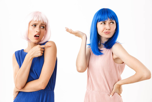 Portrait of two displeased women wearing blue and pink wigs holding and pointing finger at copyspace - Φωτογραφία, εικόνα