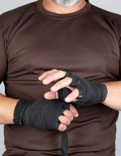 Hombre envuelve sus manos en vendaje textil negro para deportes
 - Foto, Imagen