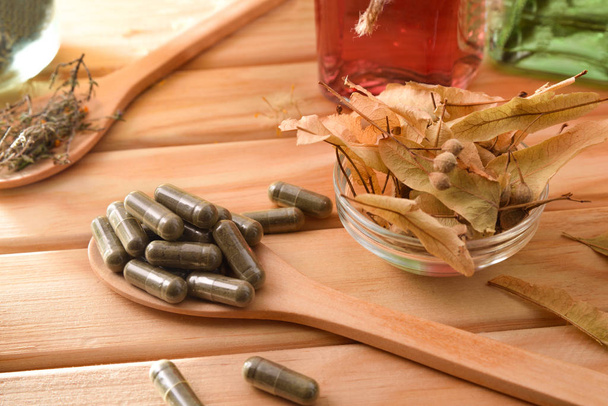 Cápsulas de medicina natural sobre cuchara de madera sobre mesa elevada
 - Foto, Imagen