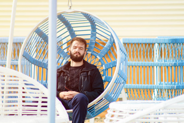 bearded young man has a rest on a swing. guy relaxes on the sun - Photo, Image