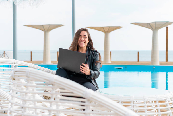 Belle fille en veste en cuir en utilisant un ordinateur portable près de la piscine. pigiste élégant au bord de la mer. étudiant. femme d'affaires
 - Photo, image