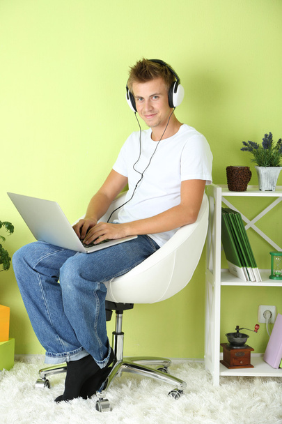 Young man relaxing with laptop in armchair, on home interior background - Фото, изображение