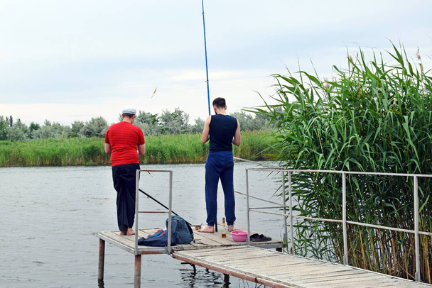 Два парня рыбачат на деревянном пирсе на озере. Люди с удочками отдыхают на природе
. - Фото, изображение