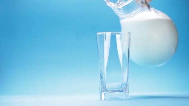 milk is poured into a glass on blue background - Πλάνα, βίντεο
