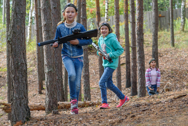 Дві дівчинки з лазерними пістолетами бігають у лісі. Laser tag - гра з гарматами, які стріляють інфрачервоними променями. Популярна гра для широкого спектру років. Однокласники бавляться надворі. - Фото, зображення