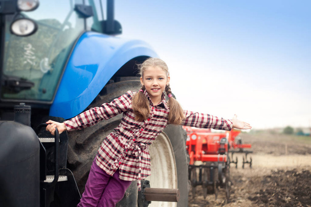 Roztomilá dívka v blízkosti moderního traktoru v terénu. - Fotografie, Obrázek