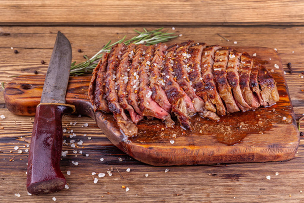 Steak de boeuf grillé tranché avec épices et couteau sur planche à découper en bois
 - Photo, image