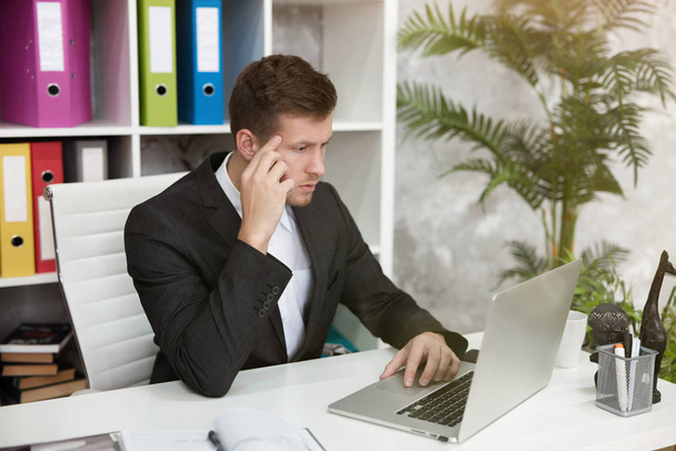 pohledný muž manažer vypadá zmateně sedí na svém pracovišti v úřadu na konci dne. multitasking, koncept práce - Fotografie, Obrázek