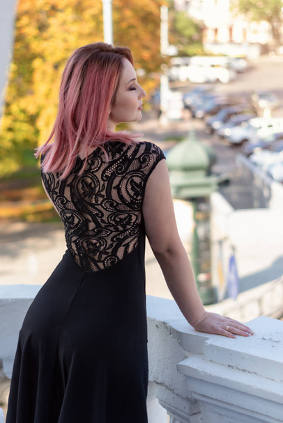 黒いドレスの赤髪の女の子がバルコニーから旧市街のロマンチックな景色を楽しんで.  - 写真・画像
