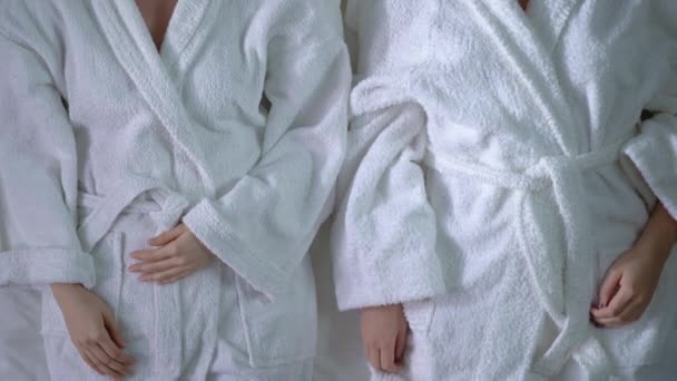 Two young ladies lying on bed in bathrobes, relaxed after beauty care procedures - Filmagem, Vídeo