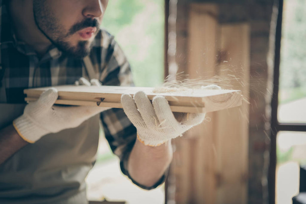 Cropped close up photo of serious confident man blowing sawdust away from wooden block before polishing - 写真・画像
