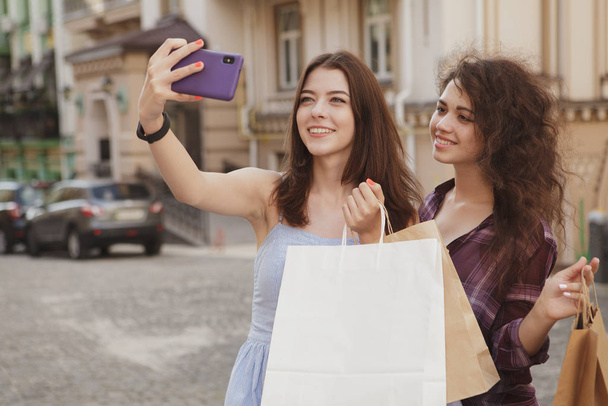 Γυναίκες φίλοι που χρησιμοποιούν έξυπνο τηλέφωνο ενώ περπατούν στους δρόμους της πόλης - Φωτογραφία, εικόνα