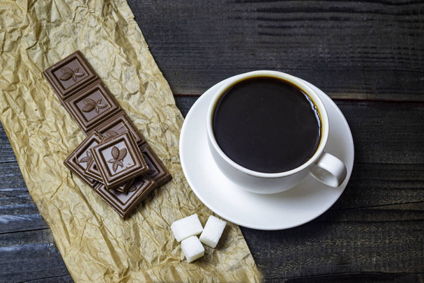 white cup with coffee and chocolate on a black background, top view, selective focus - Foto, Imagem