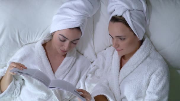 Girls reading lifestyle magazine in bed curious about fashion news, pajama party - Filmmaterial, Video