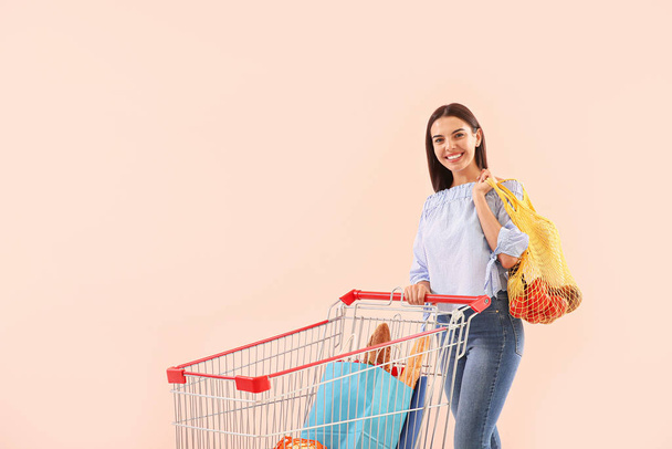 Young woman with shopping cart on color background - Foto, Bild