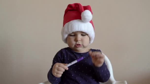 Baby in santa hat playing with felt pens. Coloring a book. Creative activity. Indoors celebrating - Materiaali, video