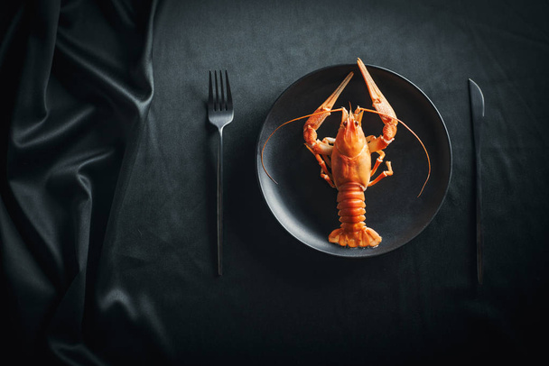 Top view of cooked lobster on plate with cutlery served on tablecloth on table in black color - Photo, image