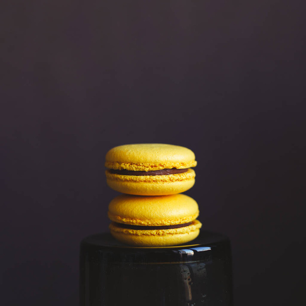Two yellow french macarons on dark background. Banana macarons with chocolate cream.   - Zdjęcie, obraz
