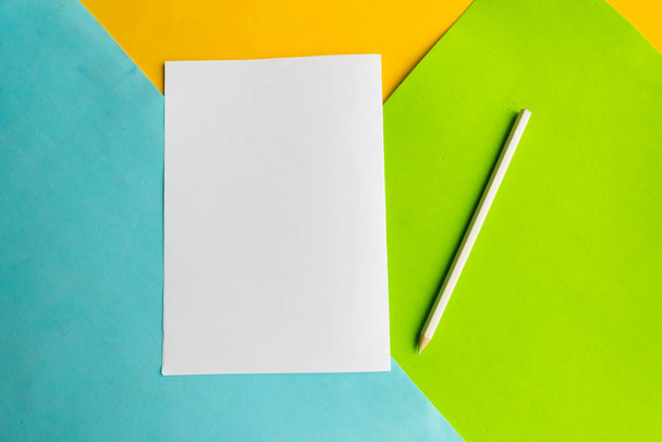 Biała makieta pusta i ołówek na geometrycznym niebieskim, zielonym i żółtym tle - Zdjęcie, obraz