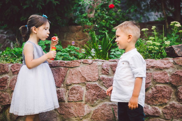 Two children in the park blowing soap bubbles and having fun. Two baby Playing With Soap Bubbles. brother and sister having fun outdoors, happy childhood concept - Photo, Image