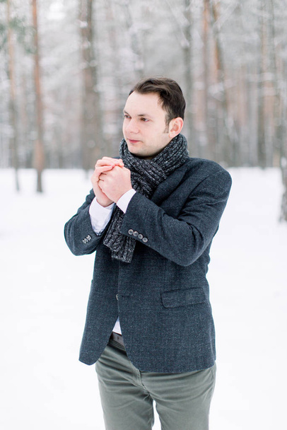 Young handsome groom walking in snowy forest, outside in winter. Winter Frost. Happy Man Rubbing Hands To Warm Up Looking At Camera Standing In Snowy Forest - Фото, изображение
