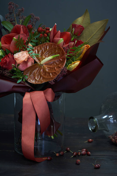 Chic autumn bouquet in red colors in vintage style in a glass vase and a huge jar of dry rose hips on a dark background, selective focus - Foto, afbeelding