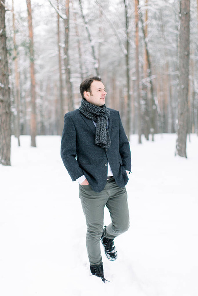 Handsome hipster man groom wearing a stylish suit, standing in the winter snowy forest, full length photo - Foto, Imagen